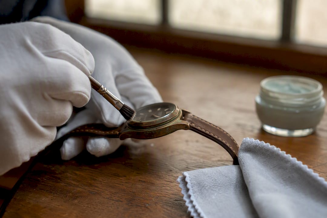 Gloved hand brushing verdigris off bronze watch case