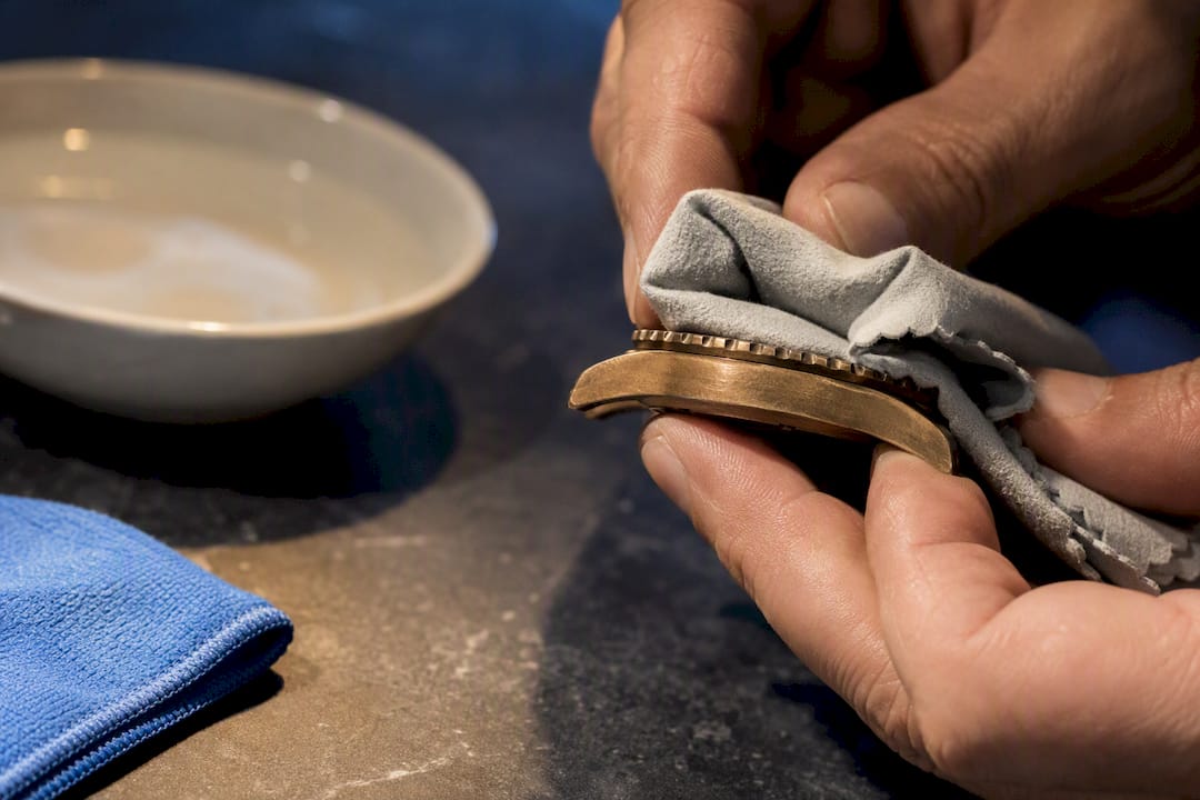 Hands cleaning an anonymous bronze watch case