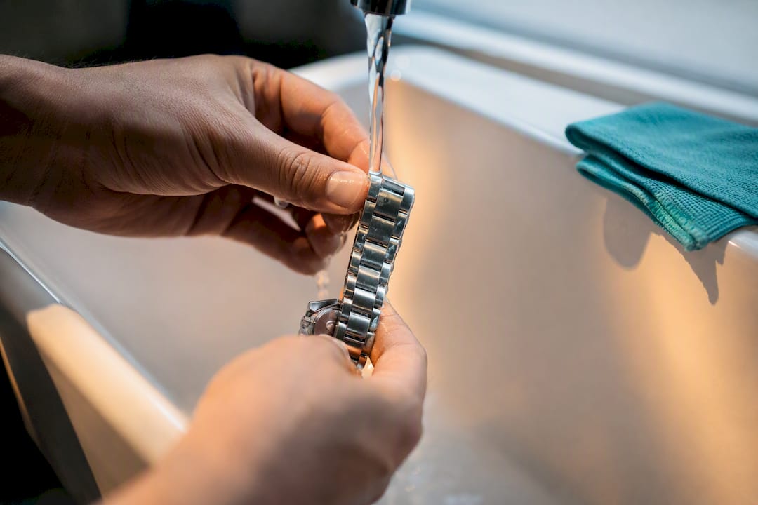Hands rinsing an anonymous metal watch bracelet